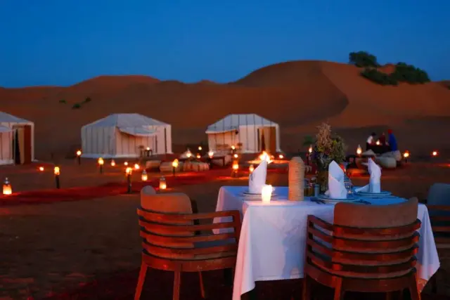 Mesa romántica para dos con faroles sobre la arena de Merzouga al caer la noche